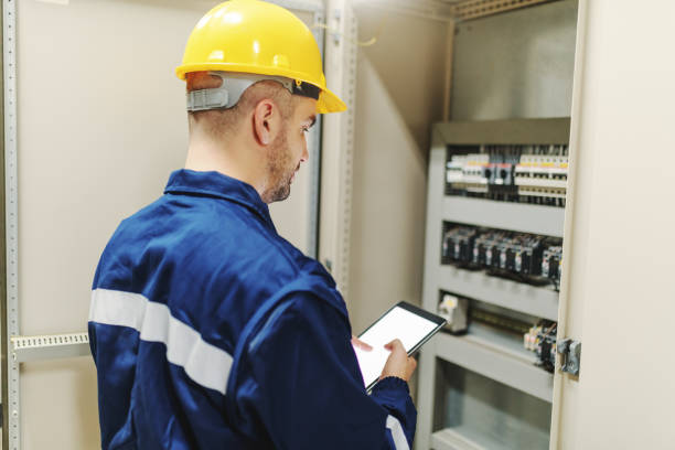 istock Electrician in protective suit and helmet using tablet and trying to fix glitch while standing next to dashboard in heavy industry plant. 1138607161