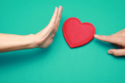 Mans finger pushing red heart to woman,women's hand showing protest to love and show stop with hand isolated on green background