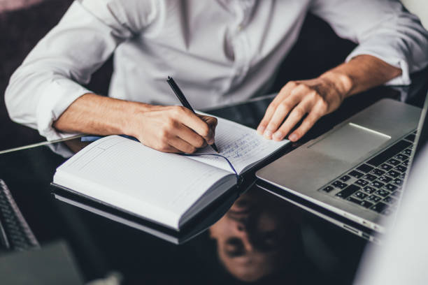 istock man sits at table,working on laptop, and makes notes in notebook. Online marketing, education, e-learning. close up 1138616229