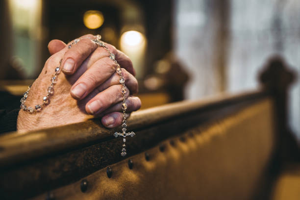 Praying hands with rosary in church stock photo