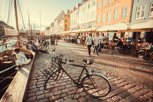 Copenhagen, Denmark - September 4, 2018: Evening sun on Nyhavn riverbank with walking people, and relaxing in restaurants of popular city leisure area on 4 September, 2018. Copenhagen has population 1.3 million