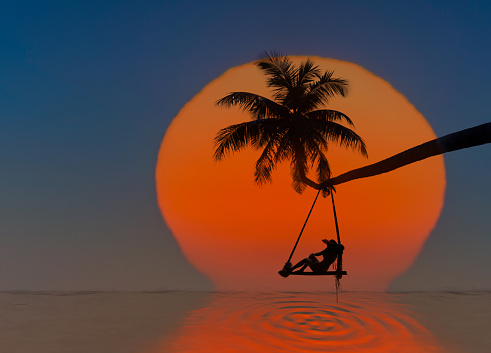 Fairy tale sunset of the large sun drop into the sea with alonely woman sitting on wooden swing under coconut plam tree over the sea beach, enjoy feel comfortable in long holidays vacation in summertime at the sea or feel alone in the sea