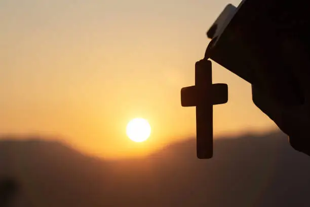 Siluette of Christian woman  holding a bible and wooden Christian cross necklace while praying to God.