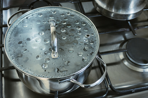 Stainless steel saucepan. Pot with a glass lid with boiling water is on the gas stove. Concept of cooking. Selective focus.
