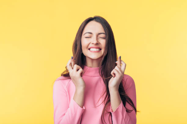 Young beautiful woman crossing her fingers and wishing for good luck over yellow background stock photo