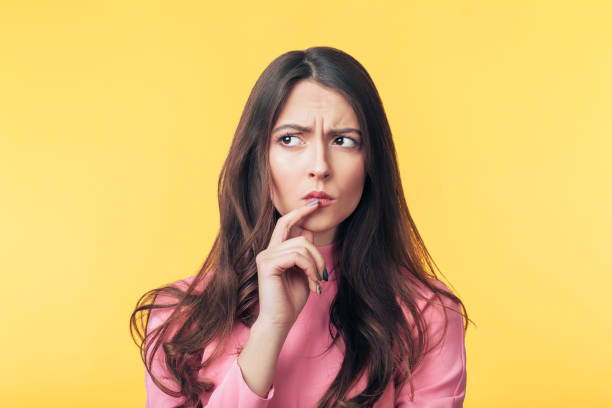 Thoughtful confused woman looking away isolated over yellow background stock photo