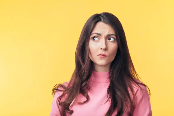 Photo of Thoughtful confused woman looking away isolated over yellow background