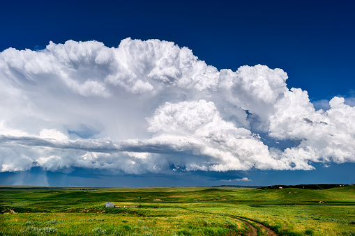Cumulonimbus thunderstorm clouds and blue sky with rolling, green grass hills and Wyoming landscape.