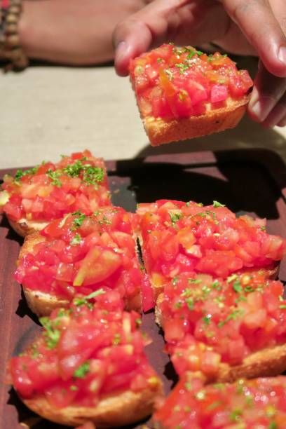 Image of bruschetta at Italian restaurant with herbs, tomato on bread served on wooden platter, healthy snack on dining table, starter appetiser dinner Italian bruschetta served on a wooden platter at an italian restaurant. A healthy snack with tomatoes, bread and herbs, a healthy snack as a starter or appetiser eaten before dinner appetiser stock pictures, royalty-free photos & images