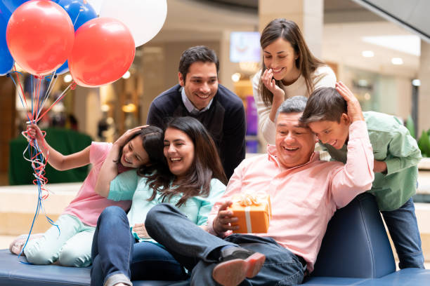 Happy grandfather celebrating Fatherâs Day with his family at the mall Happy grandfather celebrating Fatherâs Day with his family at the mall and holding a gift while smiling â lifestyle concepts father son grandfather fathers day stock pictures, royalty-free photos & images