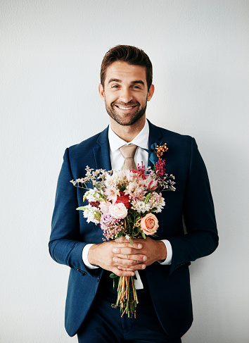 Studio shot of a handsome young groom holding a bunch of flowers a gray background