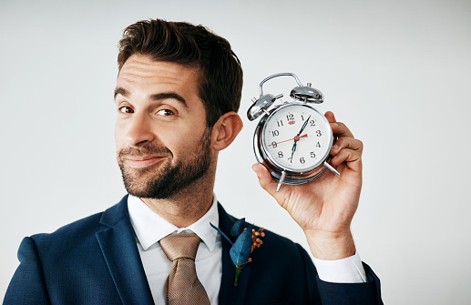 Studio shot of a handsome young groom holding a clock against a gray background