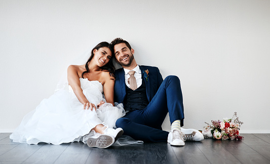 Studio shot of a newly married young couple sitting together on the floor against a gray background