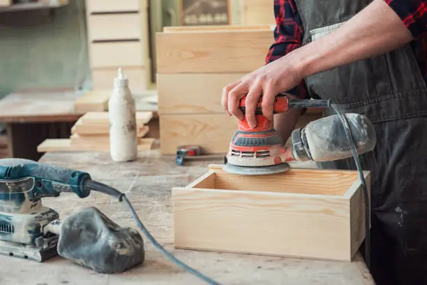 Worker grinds the wood box of angular grinding machine