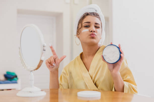 istock Cute girl is getting ready to start her day. She uses a moisturizer on her face. During this she has a towel on her head. 1138648062