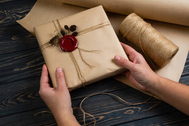 processus de paquet cadeau enveloppé dans du papier de métier, attaché avec la ficelle et le sceau de cire collé sur le fond noir en bois - wrapped package string box photos et images de collection