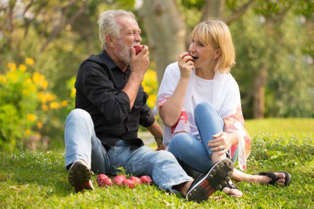 Happy senior couple relaxing in park eating apple together morning time. old people sitting on grass in the autumn park . Elderly resting .mature relationships. family stock photo