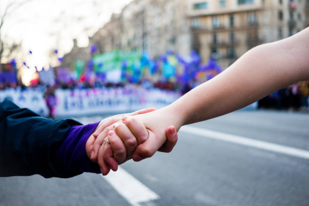 young women holding hands during woman's day rally with purple balloons in background for women rights and feminism stock photo