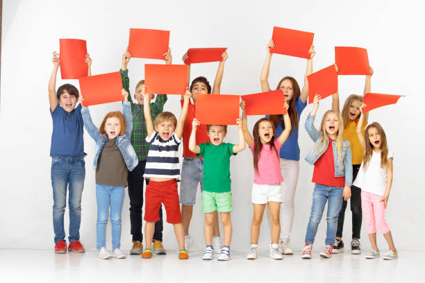 Group of children with a red banners isolated in white Group of happy screaming children with a red empty banners isolated in white studio background. Education and advertising concept. Protest and childrens rights concepts. childrens rights stock pictures, royalty-free photos & images