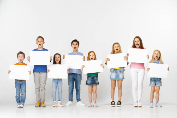 Group of children with a white banners isolated in white Group of happy surprised screaming children with a white empty banners isolated in light studio background. Education and advertising concept blackboard child shock screaming stock pictures, royalty-free photos & images