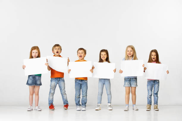 Group of children with a white banners isolated in white Group of angry screaming children with a white empty banners isolated in white studio background. Education and advertising concept. Protest and childrens rights concepts. blackboard child shock screaming stock pictures, royalty-free photos & images