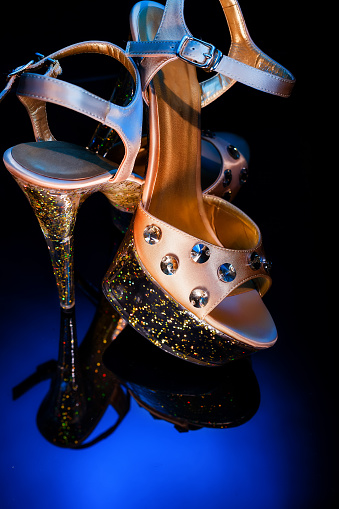 High-heeled shoes for dancing and striptease stand on a glass reflective surface. Champagne-colored shoes with round stones. Pole dancing