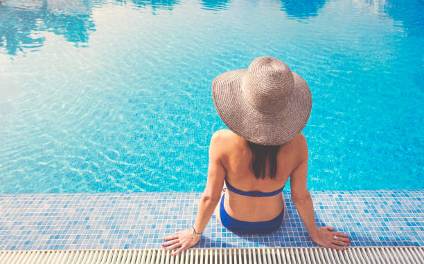 красивая женщина отдыхает в бассейне с солнцем шляпу - poolside enjoyment sensuality blue стоковые фото и изображения