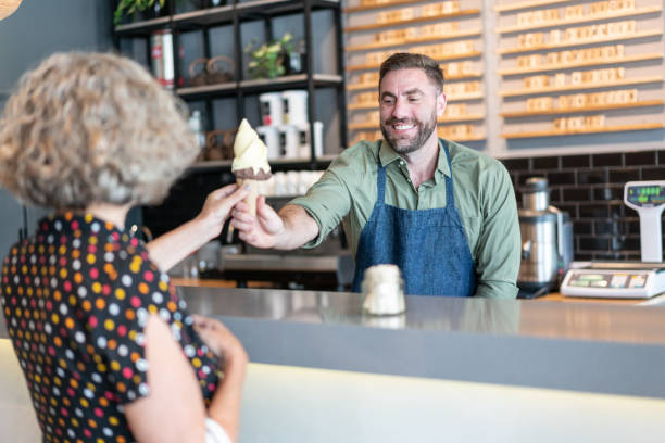travailleur amical au salon de crème glacée remettant une crème glacée au sourire de femme aîné - ice cream parlor photos et images de collection