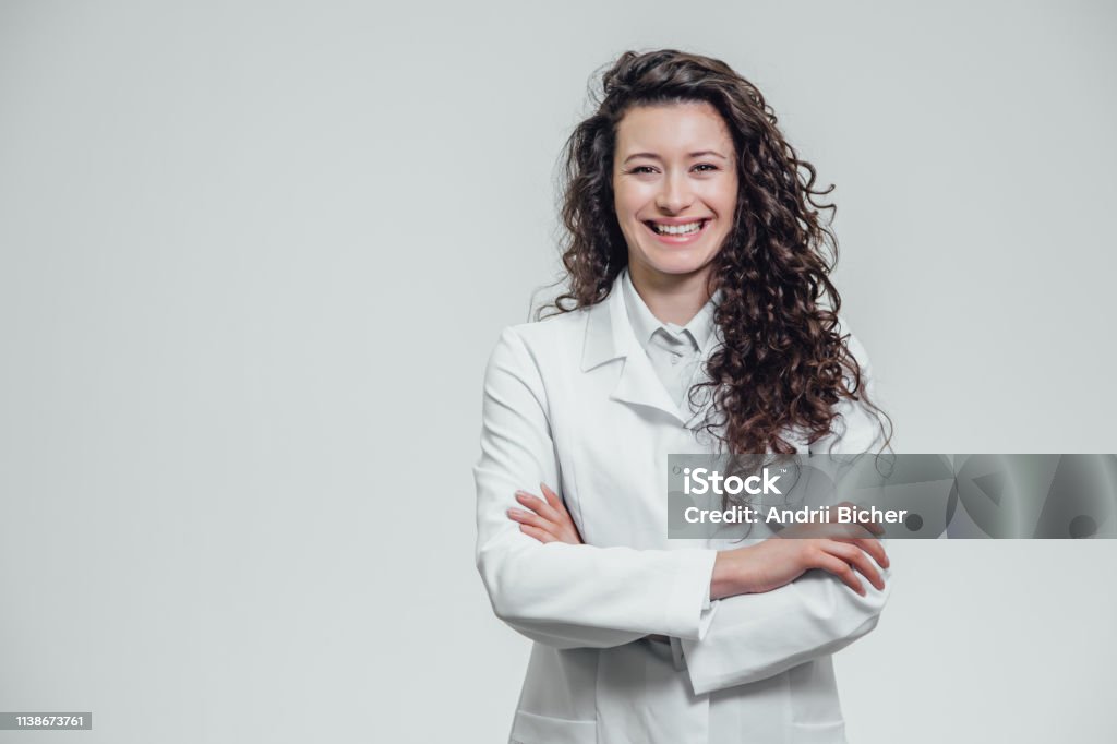 행복 한 젊은 웃는 여자 의사의 초상화입니다. 흰 옷을 입고. 회색 배경의 교차 된 손으로 균등 하 게 서 있습니다. - 로열티 프리 약사 스톡 사진
