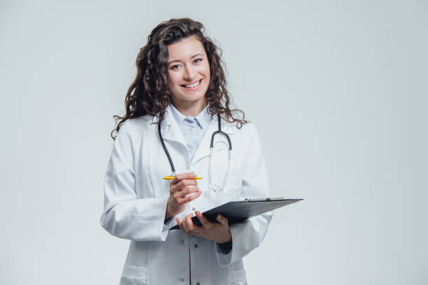 istock A young female doctor is on a gray background. During this, she keeps a folder with documents and thinks to write there. Displaying one of the items. 1138674571
