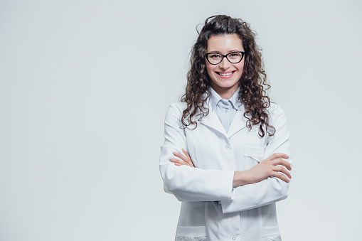 Portrait of smiling young female doctor. Beautiful brunette in white medical gown in glasses. Holding without a stethoscope on a gray background. The concept of medicine.