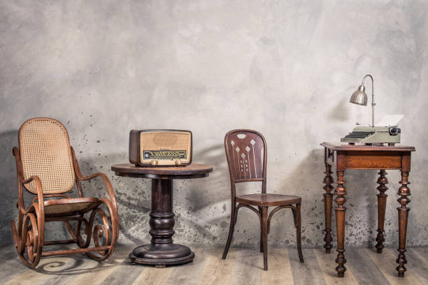 vintage loft room with antique rocking chair, broadcast radio, old typewriter and lamp on oak wooden desk front concrete wall background with shadows. retro style filtered photo - writing typewriter 1950s style retro revival imagens e fotografias de stock