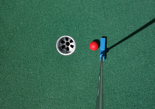 Putter and red ball near the hole on a miniature golf course