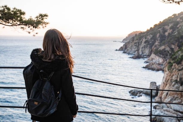istock Woman looking at sunset on rocky cliff coastline 1138681391