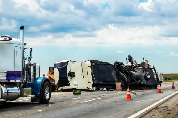 Photo of Fifth wheel RV overturned on highway with wench truck trying to get it off the road and two semis parked nearby and traffic cones keeping traffic away
