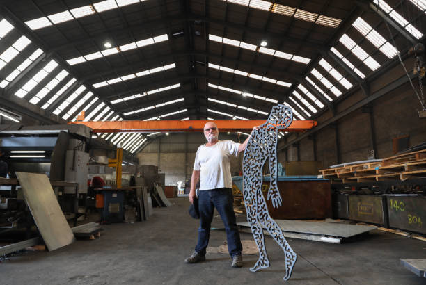 A Senior artist posing with his metal sculpture after it has been cut out of a single piece of metal using a plasma cutter.