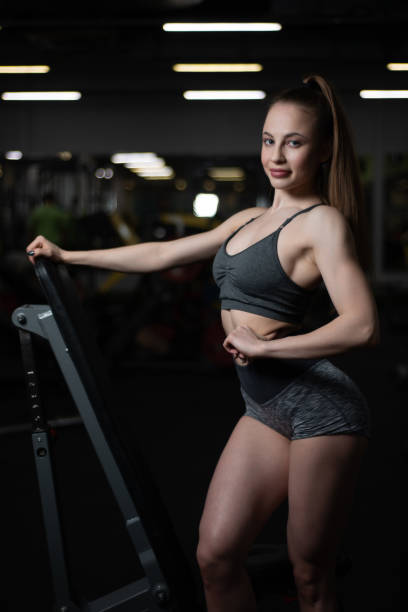 fille de remise en forme posant dans la salle de gym sur le banc montrant son corps - showing off muscular build the human body human muscle photos et images de collection