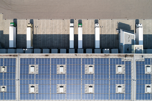 Semi trucks being unloaded at warehouse with solar panels on the rooftop, aerial view.