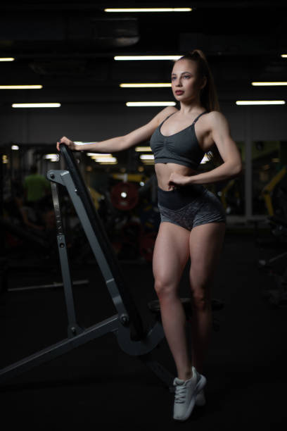 fille de remise en forme posant dans la salle de gym sur le banc montrant son corps - showing off muscular build the human body human muscle photos et images de collection