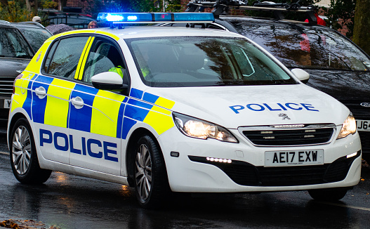 Greater Manchester Police vehicle with blue lights on closes off a road in Salford UK to allow Remembrance Day marchers to pass.