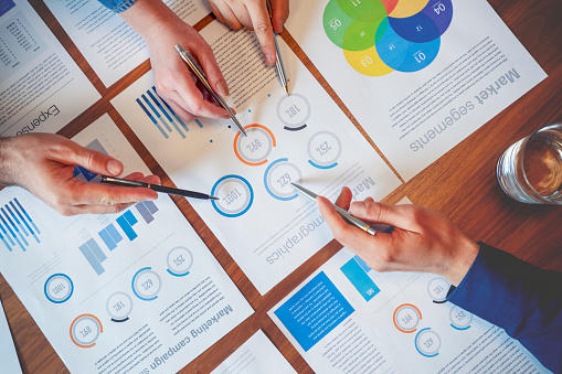 Team of business people point to numbers on financial data. Teamwork concept paperwork and graphs and charts. High angle view of hands using pens to point.