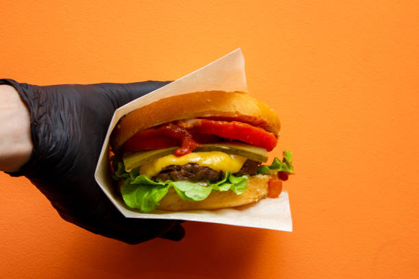 istock fresh tasty burger in the hand on orange background 1138706187