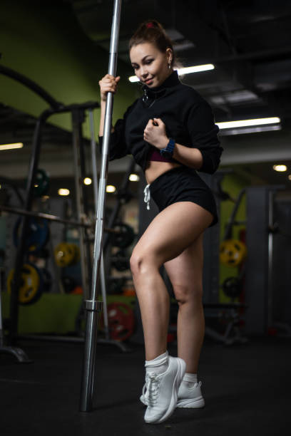 fille posant dans la salle de gym, exhibant son corps, tenant un barbell - showing off muscular build the human body human muscle photos et images de collection