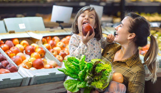 スーパーマーケットの家族。美しい若いお母さんと彼女の小さな娘が笑って、食べ物を買います。 - supermarket groceries shopping healthy lifestyle ストックフォトと画像
