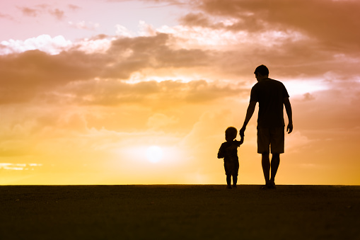 Father walking with his little son towards the sunset.