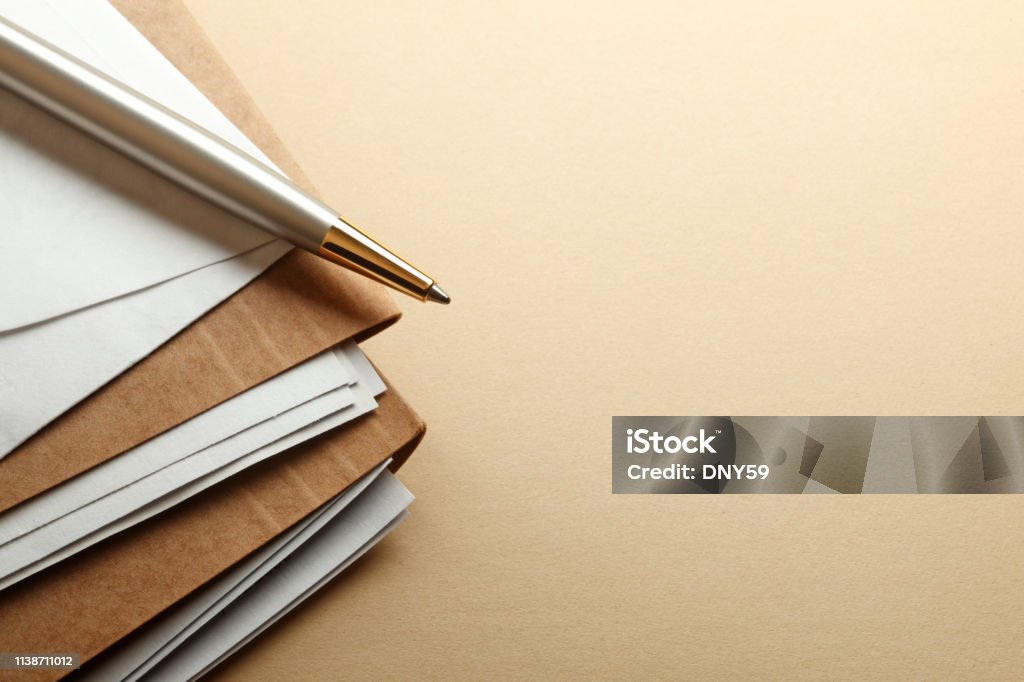 Ballpoint Pen On Stack Of File Folders A ballpoint pen rests on a stack of brown file folders. The light brown desktop provides ample room for copy and text. Document Stock Photo