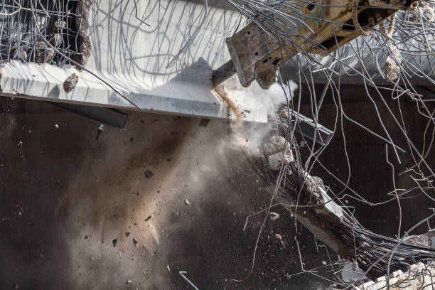 Professional demolition of reinforced concrete structures using industrial hydraulic hammer. Rods of metal fittings. Wreckage and crumbles of concrete.