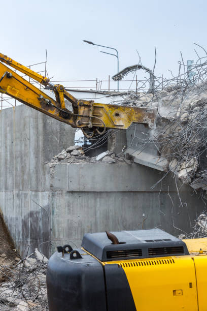 Professional demolition of reinforced concrete structures using industrial hydraulic hammer. Rods of metal fittings. Wreckage and crumbles of concrete.