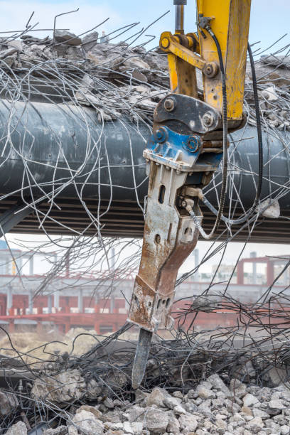 Professional demolition of reinforced concrete structures using industrial hydraulic hammer. Rods of metal fittings. Wreckage and crumbles of concrete.