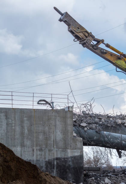 Professional demolition of reinforced concrete structures using industrial hydraulic hammer. Rods of metal fittings. Wreckage and crumbles of concrete.